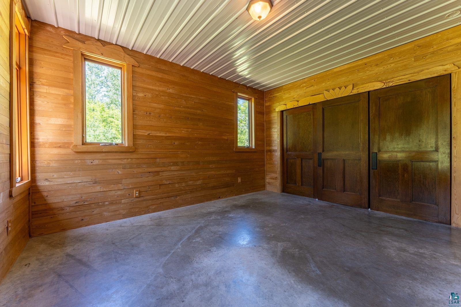 9734 Alango Road Angora, MN 55703 - Photo 14 of 41 Wood-paneled room featuring polished concrete flooring, multiple windows, a corrugated metal ceiling, and built-in wood sliding doors
