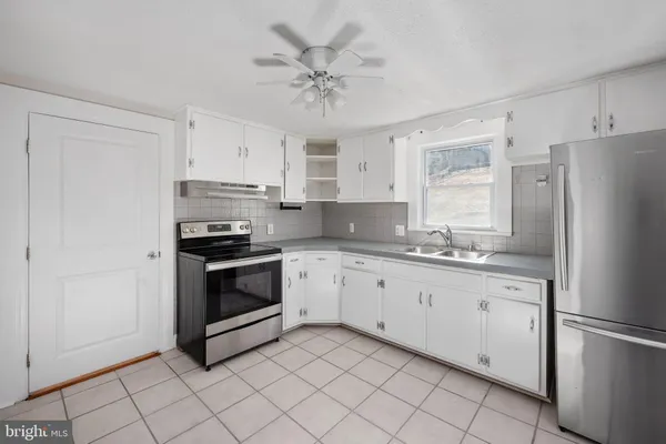 a large white kitchen with a sink a window and stainless steel appliances