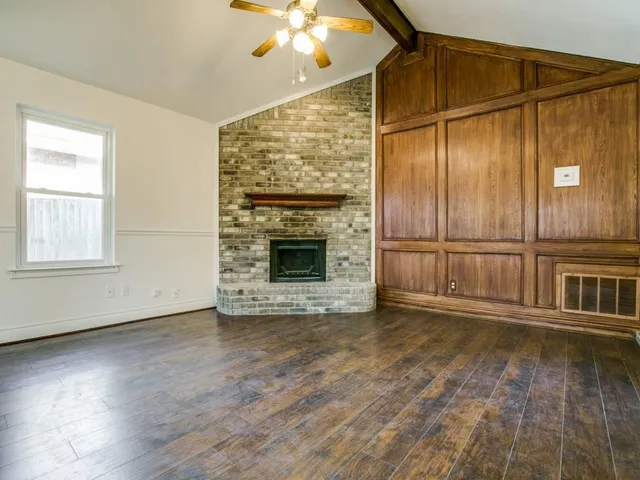 an empty room with wooden floor fireplace and windows