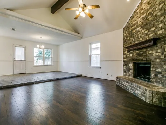 an empty room with wooden floor fireplace and windows