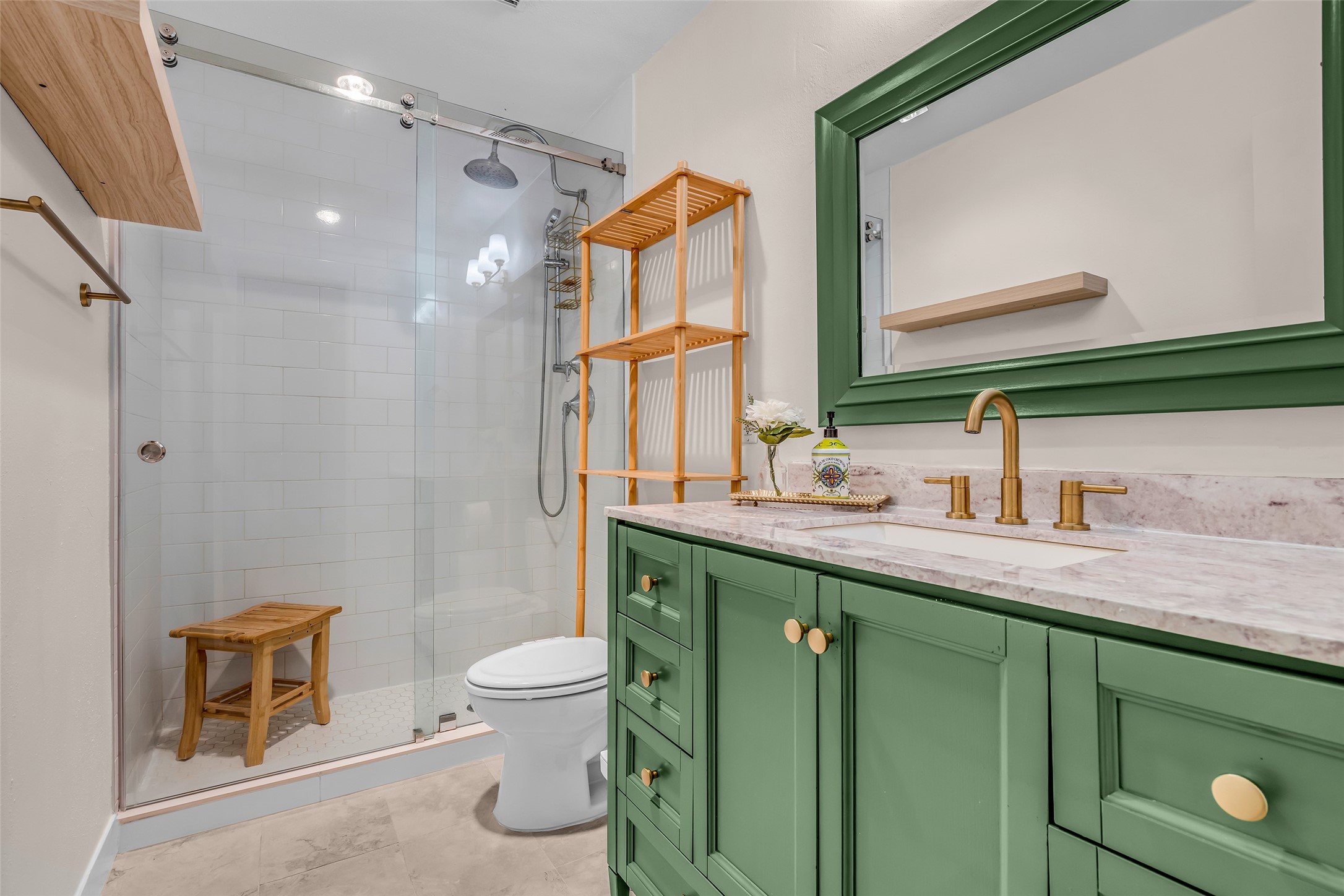 7485 Brompton Street, Unit 7485 Houston, TX 77025 - Photo 29 of 43 Primary bath features a modern design with a glass-enclosed shower and white tile backsplash. The vanity has a green finish with gold hardware, complemented by a matching framed mirror and elegant faucet add to the stylish decor.