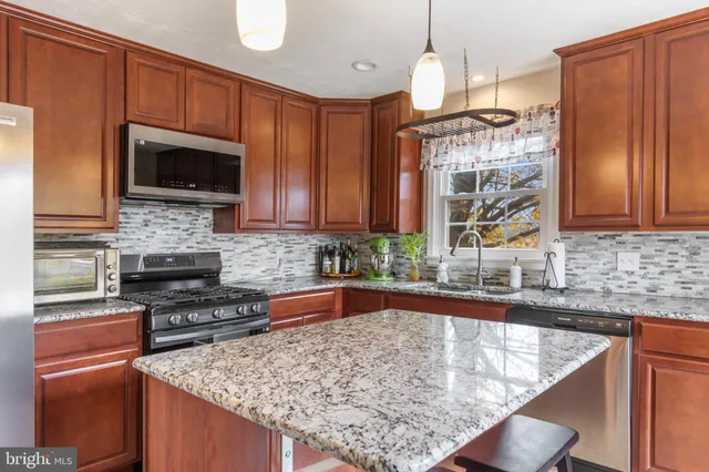 a kitchen with stainless steel appliances granite countertop a stove top oven a sink dishwasher and microwave with wooden cabinets