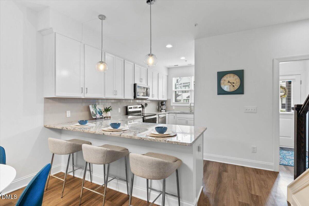 6810 Milligan Way, Unit 103 Raleigh, NC 27613 - Photo 5 of 37 a kitchen with stainless steel appliances granite countertop a sink a stove a refrigerator a dining table and chairs with wooden floor