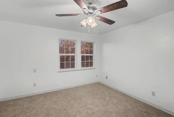 an empty room with a chandelier fan and windows