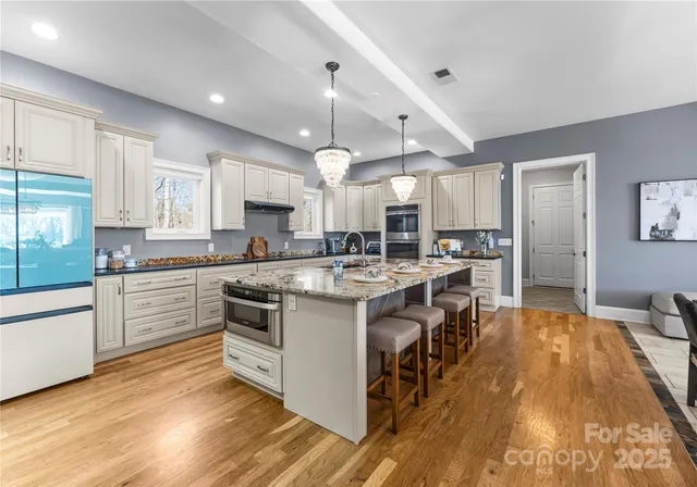 a kitchen with stainless steel appliances granite countertop a stove a sink dishwasher a refrigerator and white cabinets with wooden floor