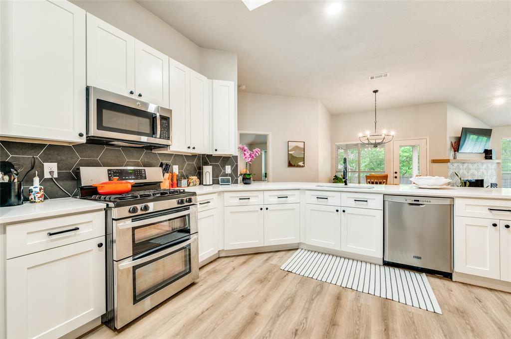 7306 Vista Ridge Lane Sachse, TX 75048 - Photo 5 of 23 a kitchen with stainless steel appliances granite countertop a stove top oven a sink dishwasher and white cabinets with wooden floor