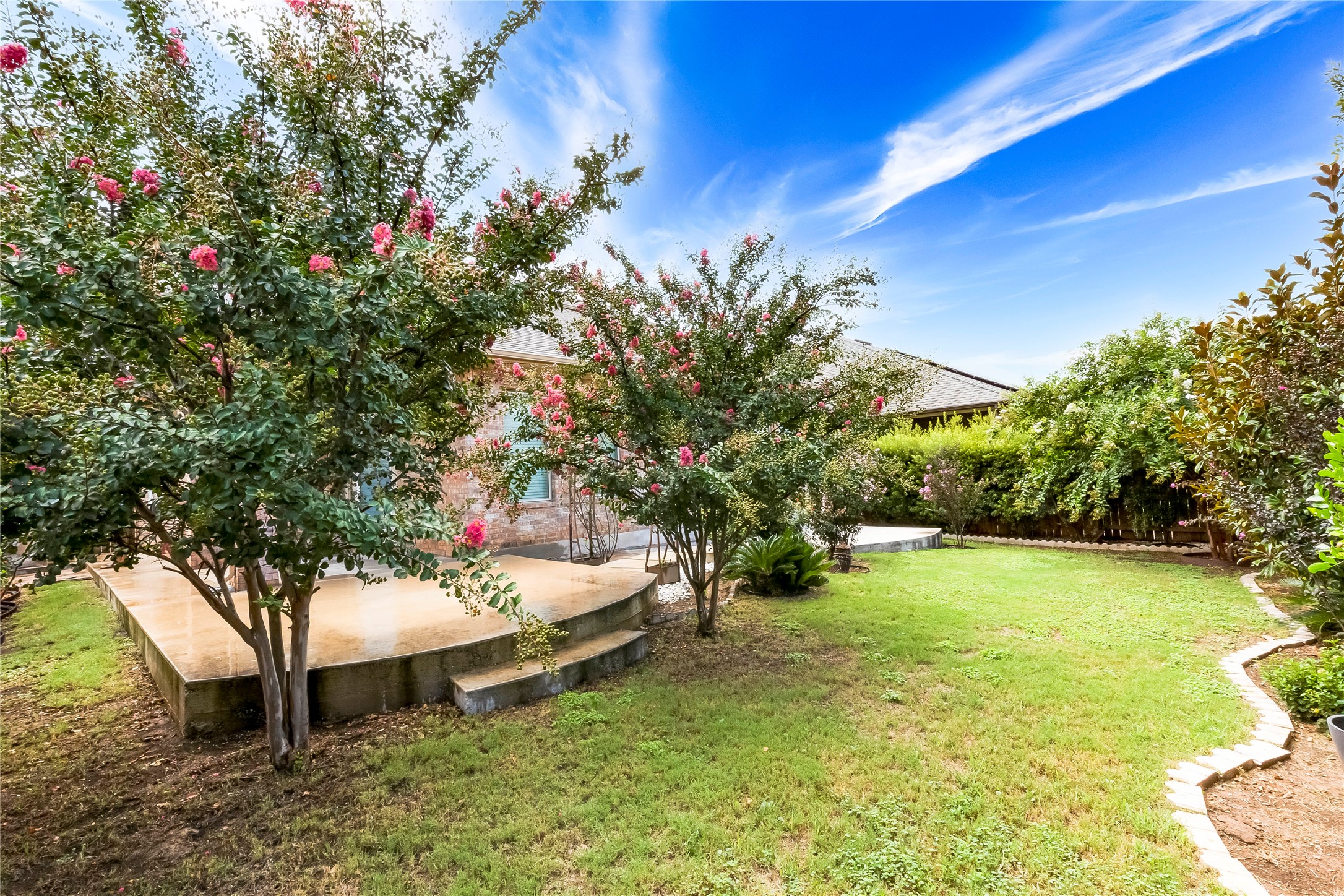 345 Fort Cobb Way Georgetown, TX 78628 - Photo 33 of 38 Lush green grass and mature flowering trees frame the elevated back concrete patio.