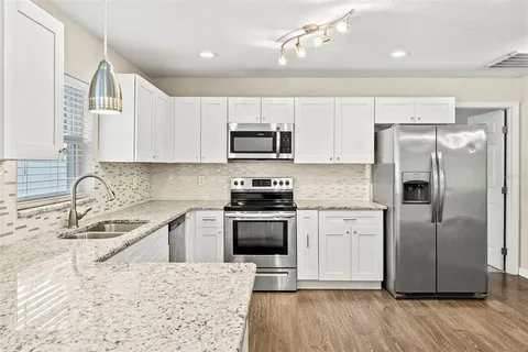 a kitchen with stainless steel appliances granite countertop a stove a sink dishwasher a refrigerator and a microwave oven with wooden floor