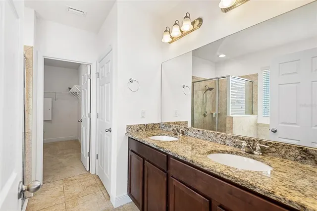 a bathroom with a granite countertop double vanity sink mirror and shower