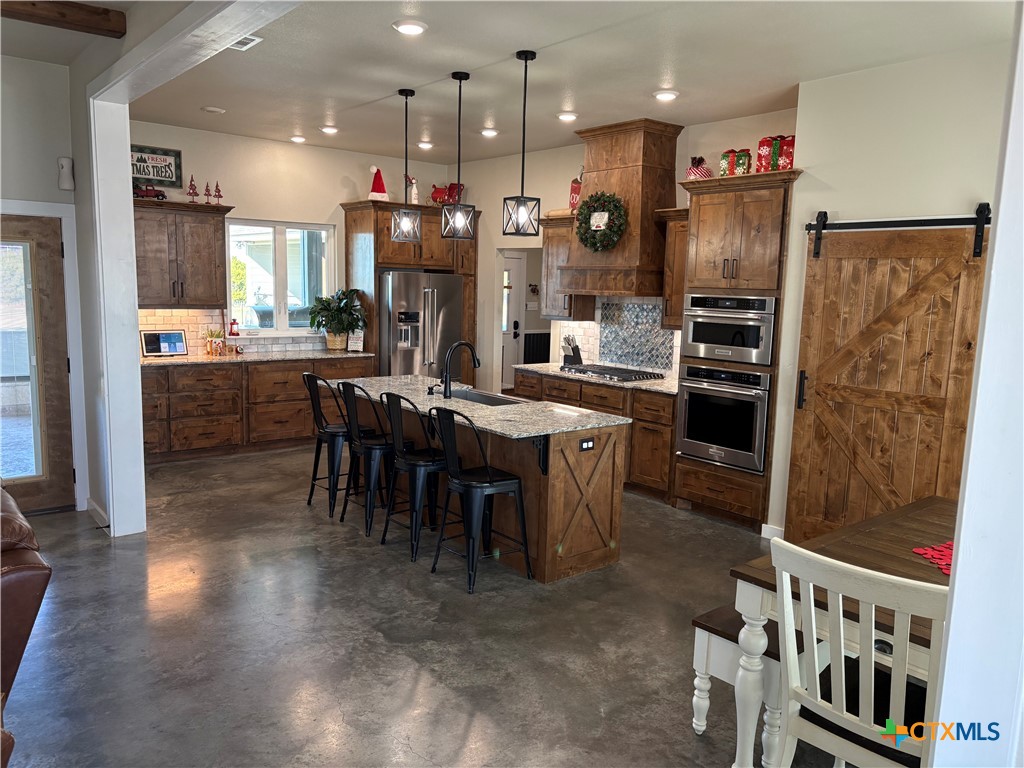 5851 Moccasin Bend Road Gatesville, TX 76528 - Photo 15 of 48 a kitchen with stainless steel appliances kitchen island granite countertop a refrigerator a stove a sink a dining table and chairs with wooden floor