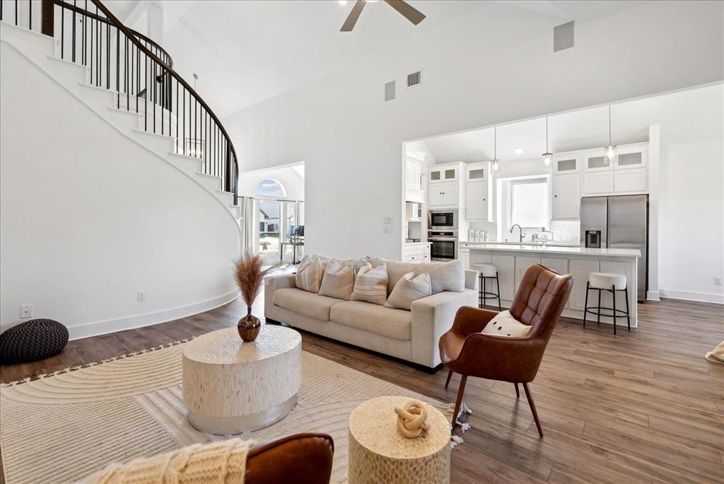 1710 Highwood Road Forney, TX 75126 - Photo 24 of 25 Open-concept living area with soaring ceilings, a sweeping staircase featuring a dark iron balustrade, wood-finish flooring, and a modern kitchen with white cabinetry and stainless steel appliances