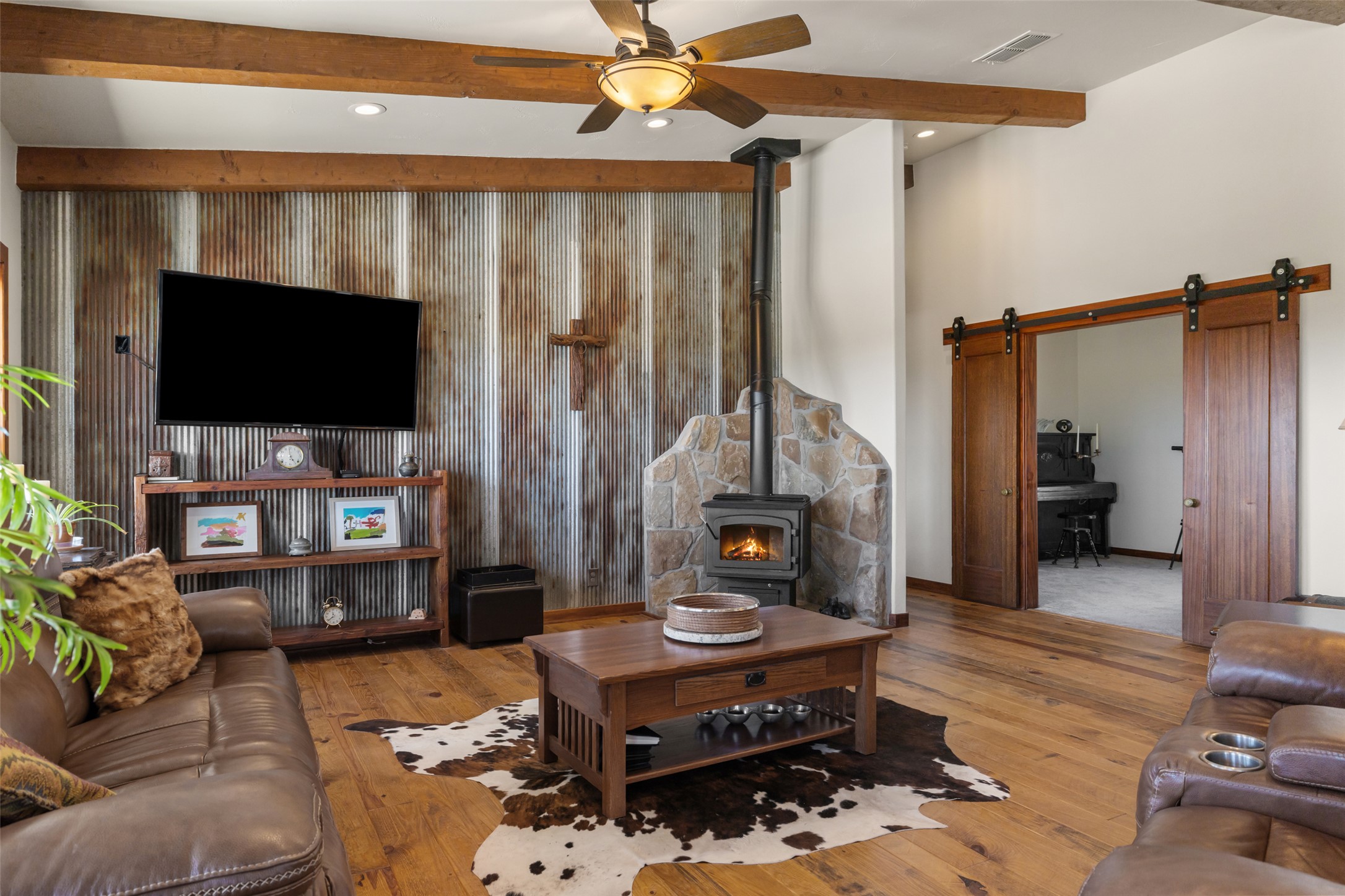 546 Lazy Oak Road Hye, TX 78635 - Photo 17 of 34 Living room featuring wood-type flooring, beam ceiling, a wood stove, a ceiling fan, and an accent wall