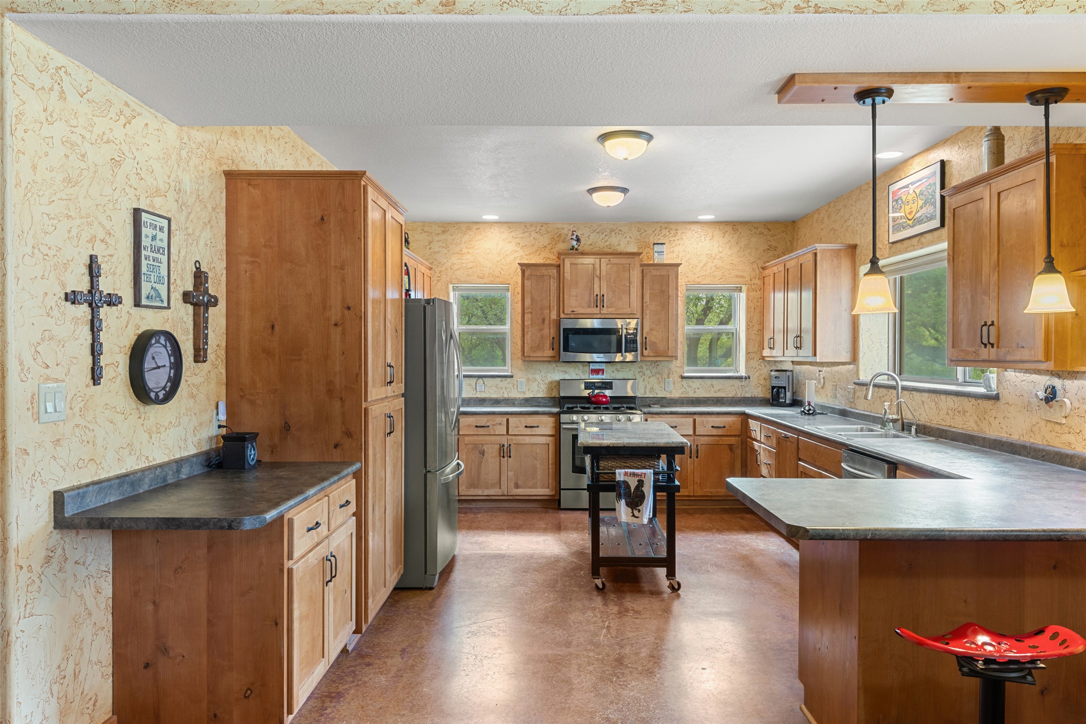 546 Lazy Oak Road Hye, TX 78635 - Photo 28 of 34 Kitchen featuring dark countertops, a peninsula, stainless steel appliances, concrete flooring, and wallpapered walls