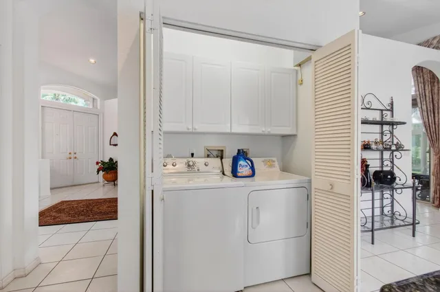 a view of a patio with dining table and chairs under an umbrella with potted plants and palm trees