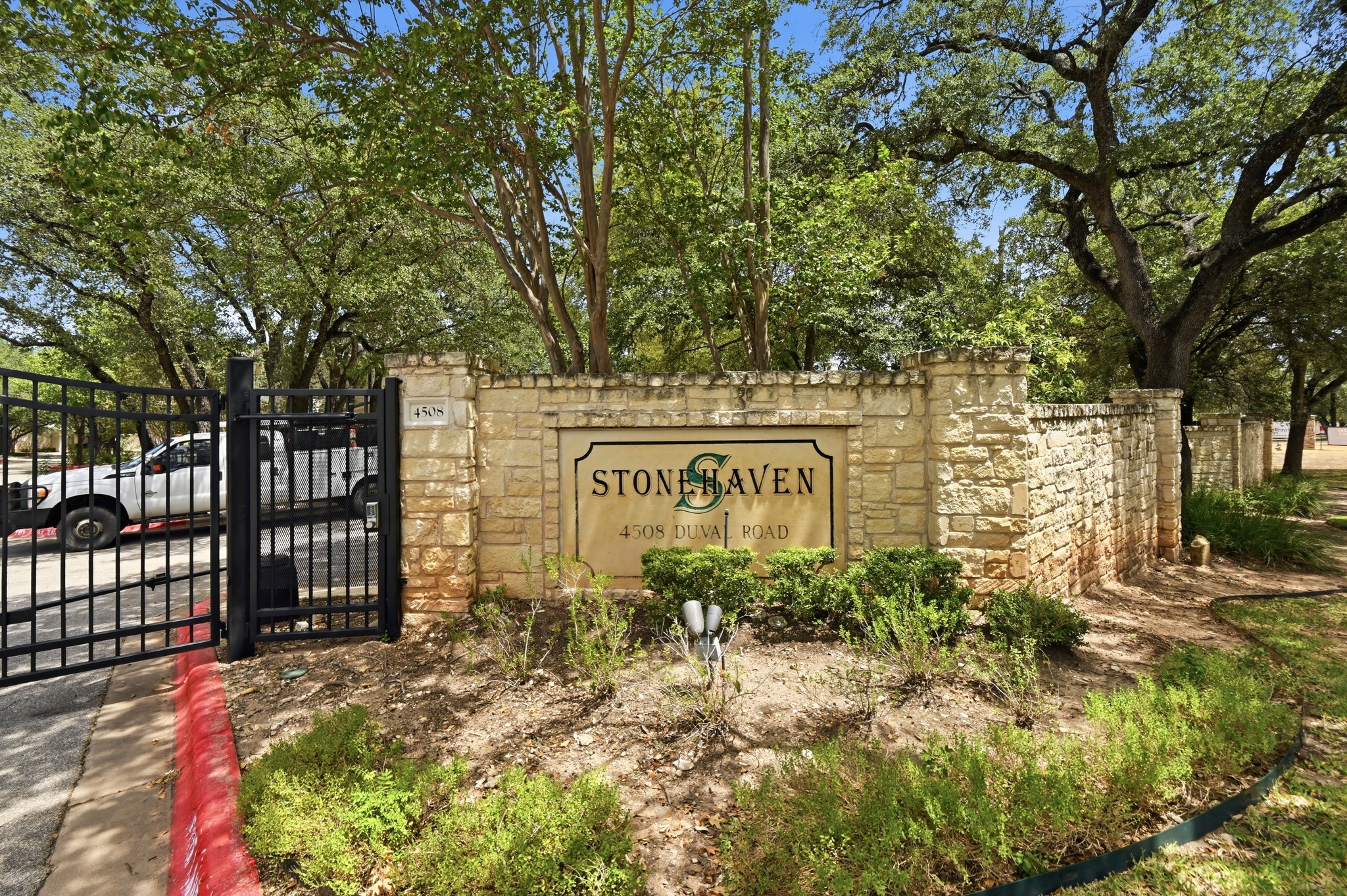 4508 Duval Road, Unit 4401 Austin, TX 78727 - Photo 23 of 26 Secure gated entryway features a stone monument sign nestled among mature shade trees.