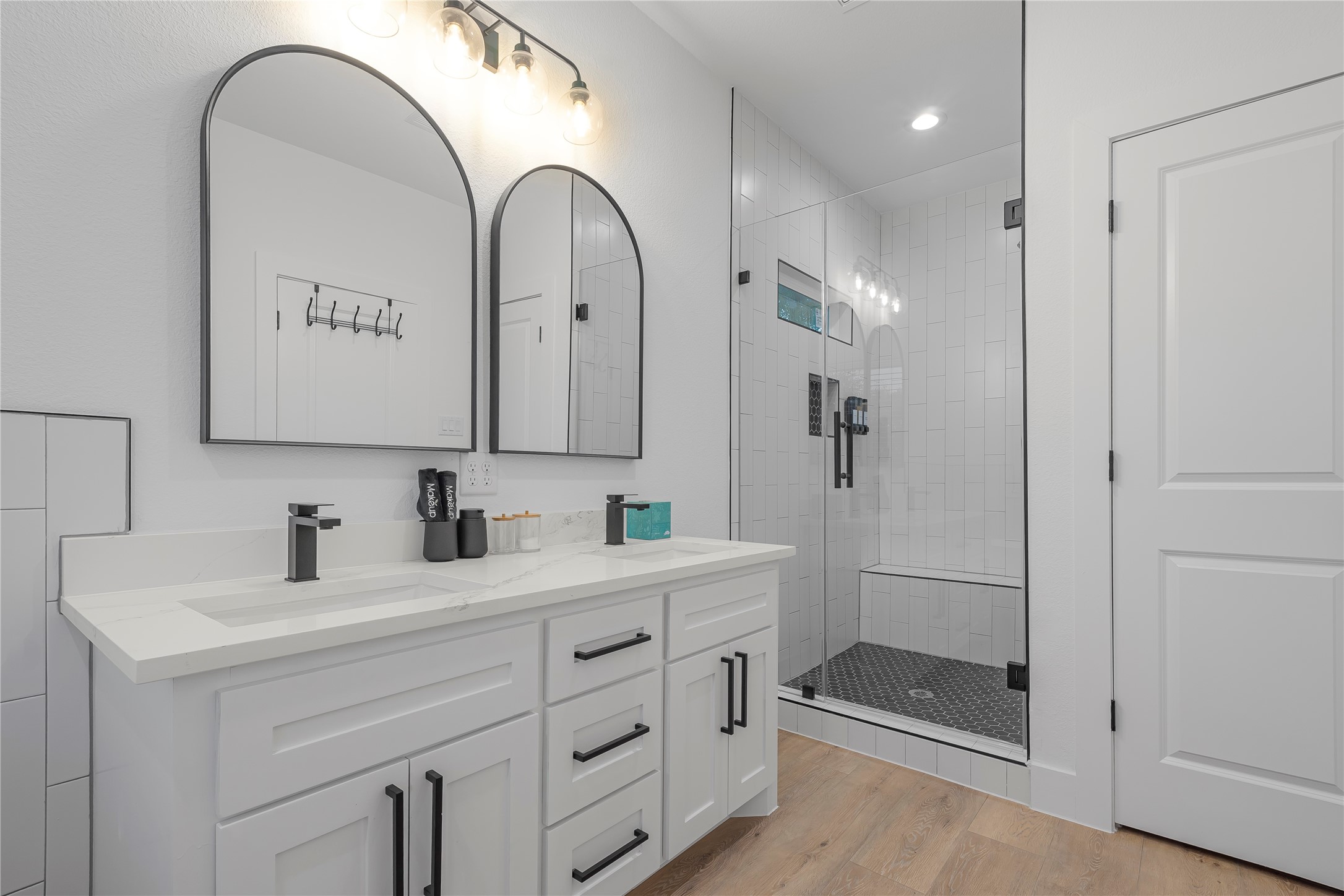 7107 Foster Street, Unit B Houston, TX 77021 - Photo 9 of 18 Sleek and modern bathroom featuring a double vanity with elegant arched mirrors, stylish black fixtures, and a spacious glass-enclosed shower with a built-in bench.
