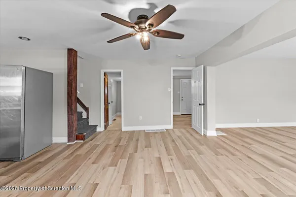 a view of an empty room with wooden floor and a ceiling fan