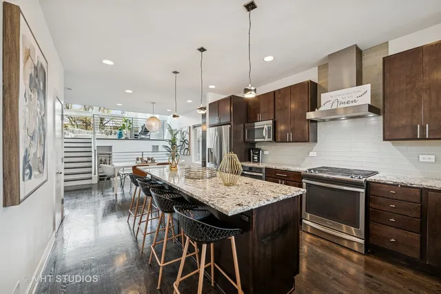 a kitchen with stainless steel appliances granite countertop a stove a refrigerator a kitchen island a dining table and chairs with wooden floor