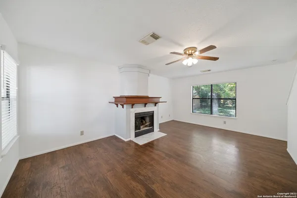 a view of a livingroom with a fireplace a ceiling fan and wooden floor