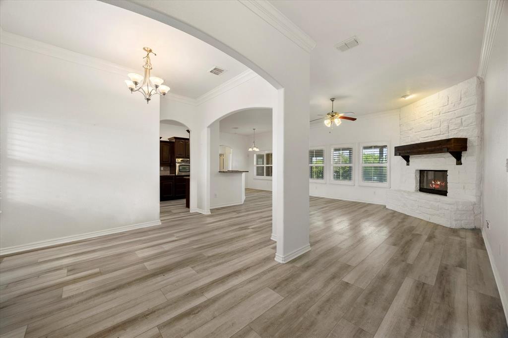 528 Hubbard Circle Nevada, TX 75173 - Photo 14 of 36 Unfurnished living room featuring ceiling fan, a chandelier, a stone fireplace, crown molding, and light wood finished floors