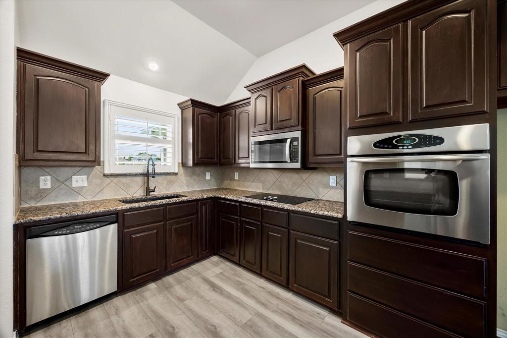 528 Hubbard Circle Nevada, TX 75173 - Photo 24 of 36 Kitchen featuring stainless steel appliances, a sink, vaulted ceiling, light stone counters, and light wood-style flooring