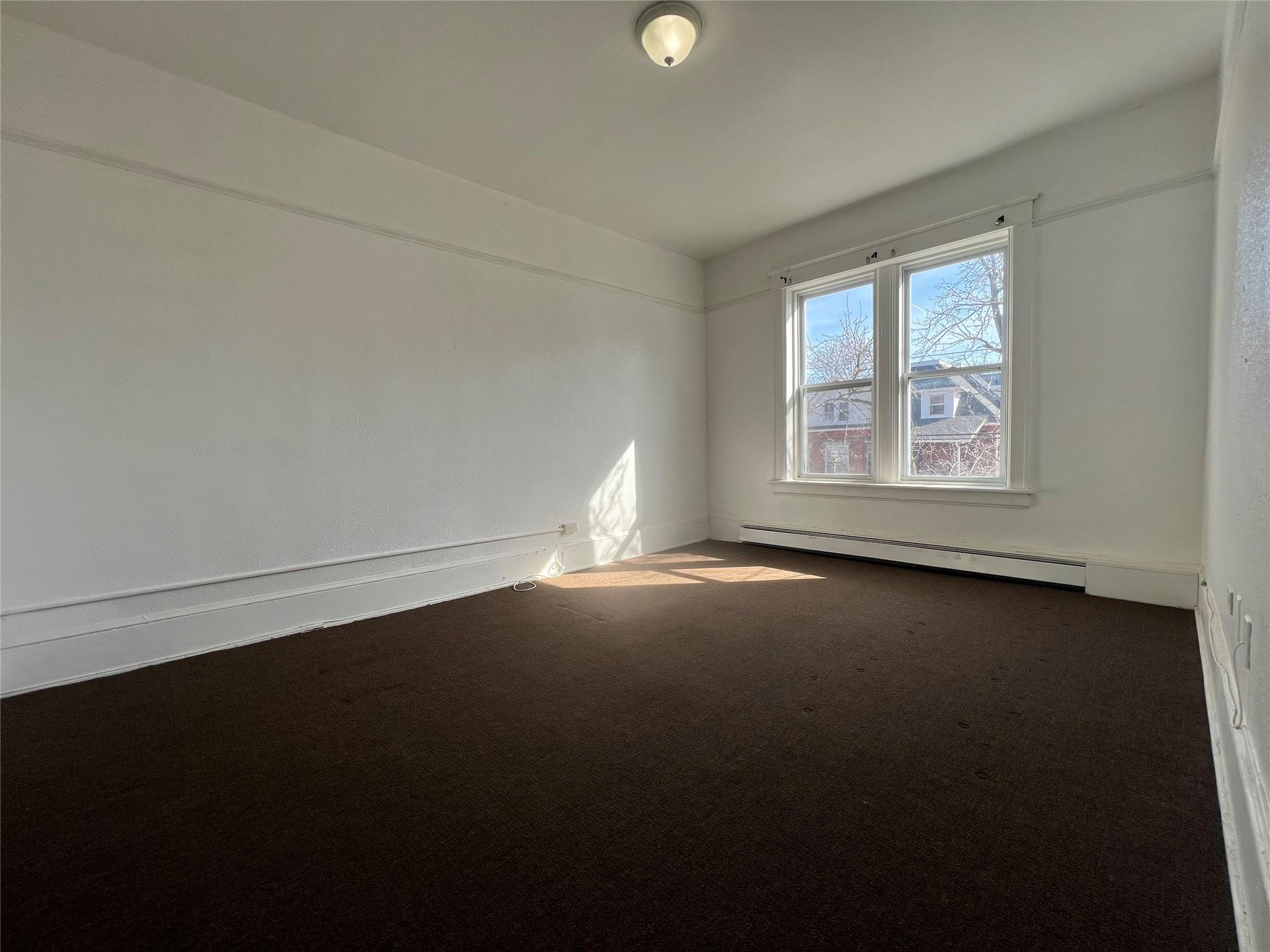 Carpeted empty room featuring a baseboard heating unit