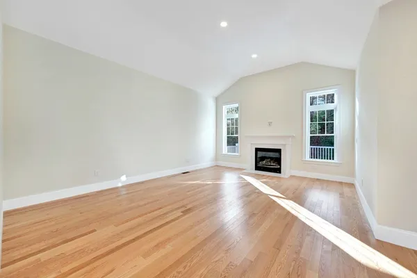 an empty room with wooden floor fireplace and windows