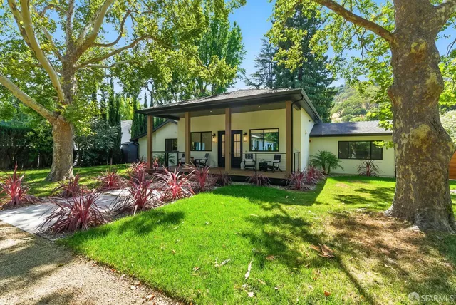 a view of a patio with table and chairs under an umbrella with large trees