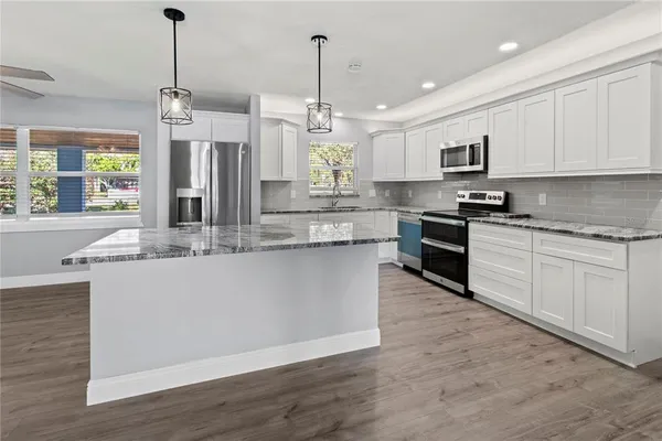 a kitchen with stainless steel appliances granite countertop a sink a stove a refrigerator and island with wooden floor