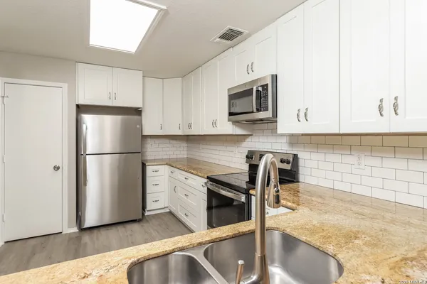 a kitchen with stainless steel appliances granite countertop a refrigerator a stove a sink a microwave and white cabinets