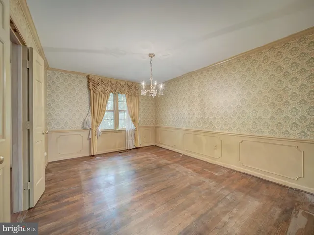 an empty room with wooden floor chandelier and windows