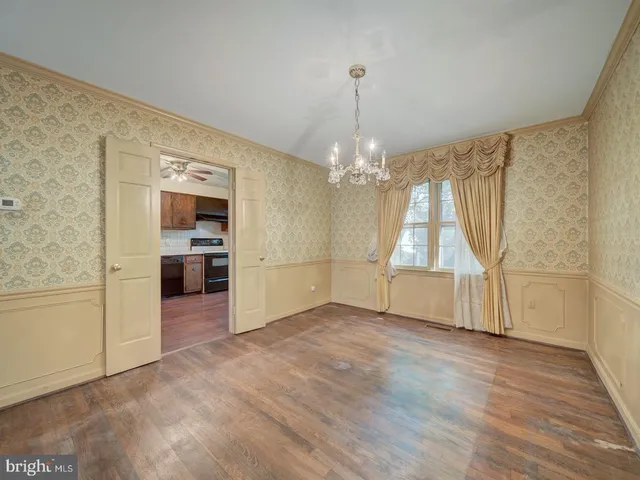 an empty room with wooden floor kitchen view and a chandelier