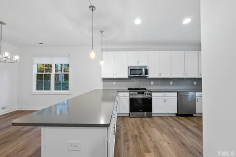 a kitchen with granite countertop a stove a sink a refrigerator and white cabinets with wooden floor