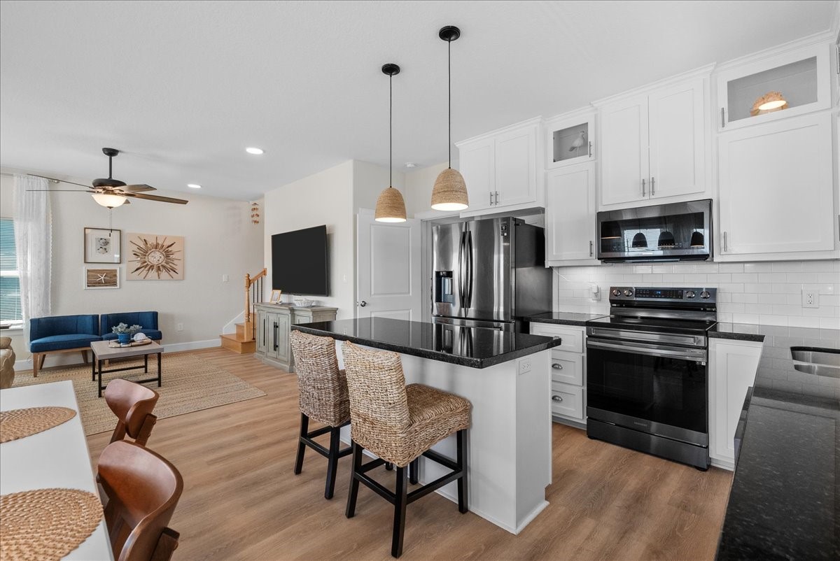 130 Beachcomber Avenue Surfside Beach, TX 77541 - Photo 11 of 33 This photo showcases a modern open-concept living space with a stylish kitchen featuring white cabinets, a countertop, and stainless-steel appliances. The adjacent living area includes cozy seating and tasteful decor, complemented by wood look flooring and ample natural light.