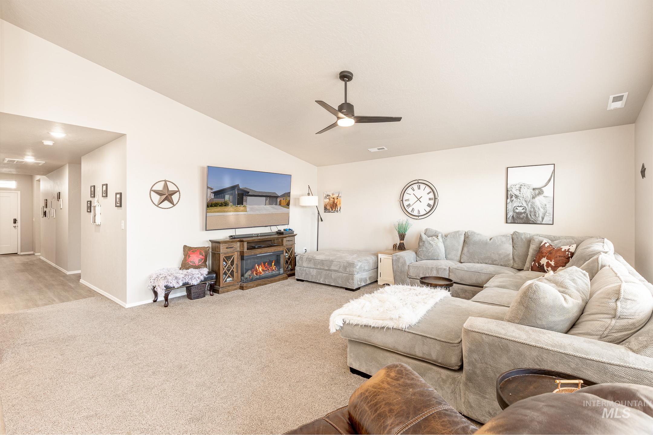 Living room with vaulted ceiling, carpet, a glass covered fireplace, and ceiling fan