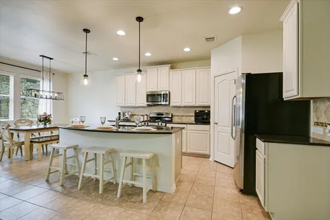 a kitchen with stainless steel appliances granite countertop a refrigerator a stove a sink a dining table and chairs