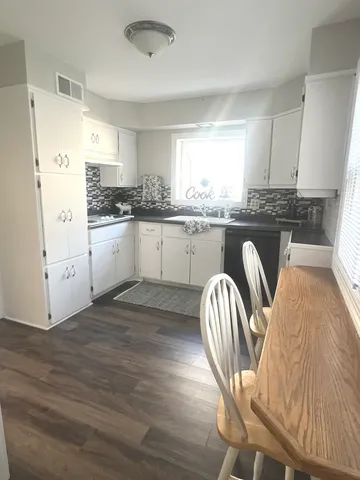 a kitchen with granite countertop white cabinets a sink dishwasher a dining table and chairs with wooden floor