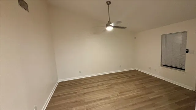 a view of an empty room with wooden floor and a ceiling fan