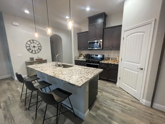 a kitchen with stainless steel appliances kitchen island granite countertop a table chairs in it and wooden floors