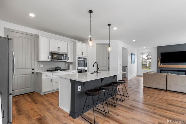 a kitchen with stainless steel appliances a stove top oven a sink dishwasher a refrigerator and white cabinets with wooden floor