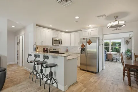 a kitchen with stainless steel appliances granite countertop a refrigerator a stove a sink a dining table and chairs with wooden floor