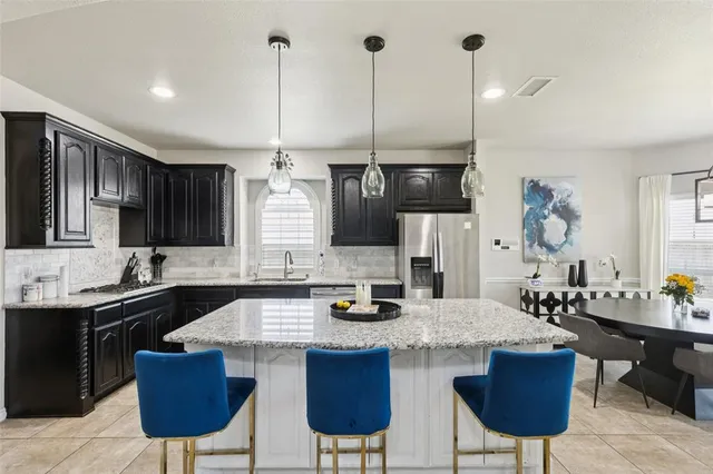 a kitchen with stainless steel appliances granite countertop a sink a stove a refrigerator a dining table and chairs