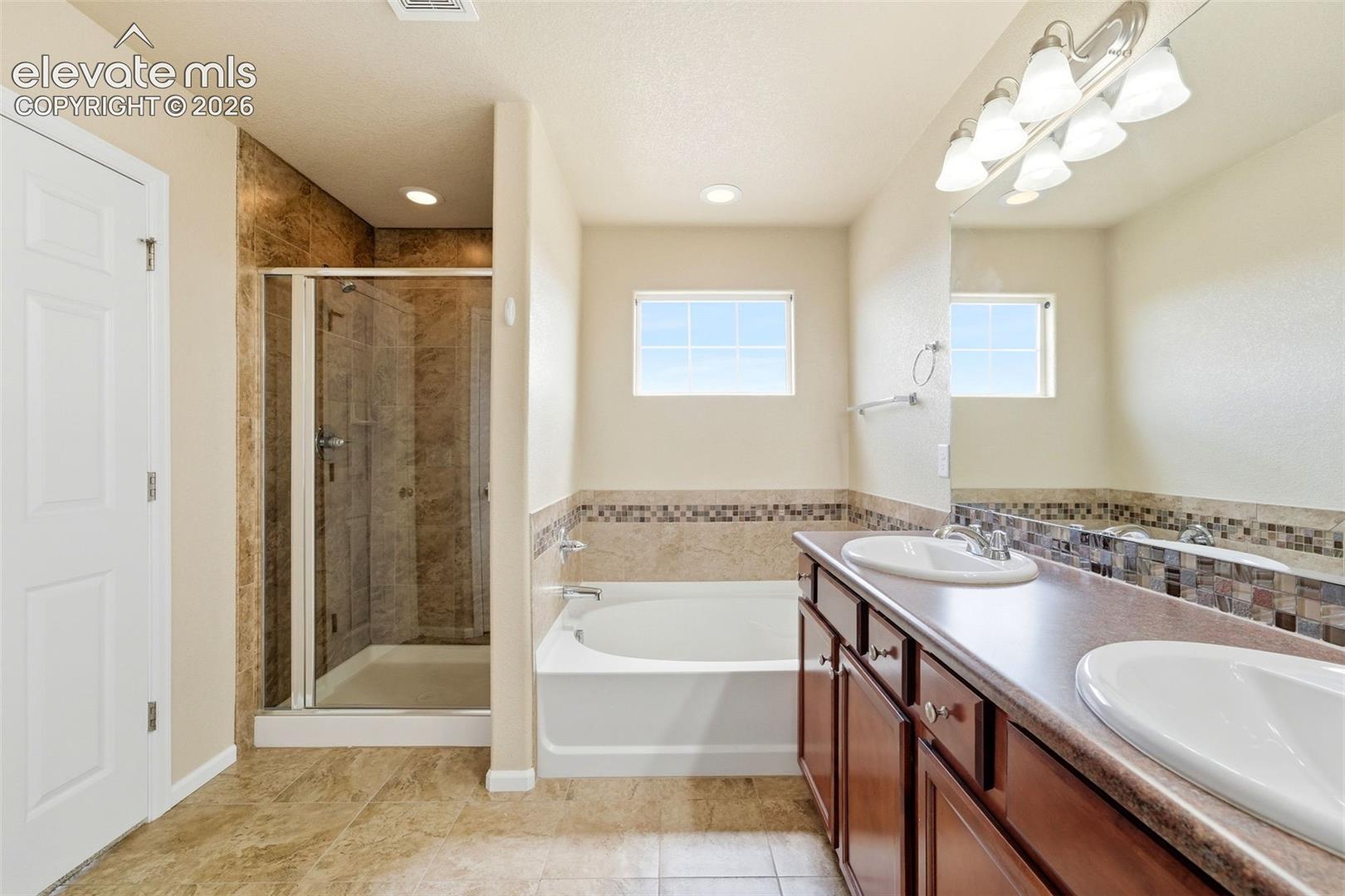 7274 Red Cardinal Loop Colorado Springs, CO 80908 - Photo 20 of 33 Bathroom featuring a dual-sink vanity, built-in bathtub, glass-enclosed shower, and tiled flooring