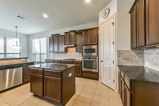 a view of a kitchen with kitchen island granite countertop a stove top oven a sink a counter space and cabinets