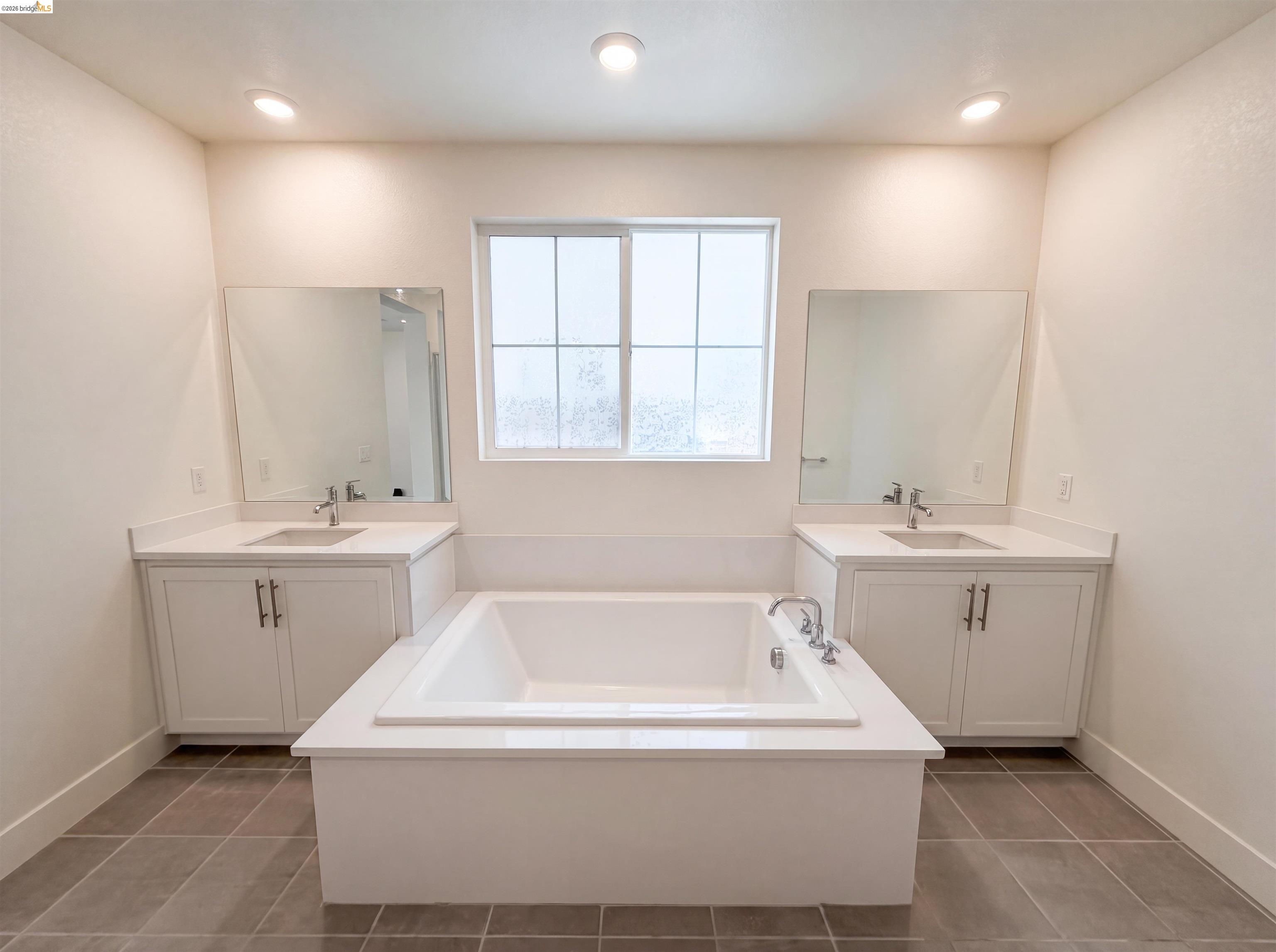 9034 Rudder Way Newark, CA 94560 - Photo 15 of 38 Recessed lighting illuminates a built-in soaking tub with chrome fixtures, flanked by two white vanity cabinets featuring undermount sinks, chrome faucets, and quartz countertops