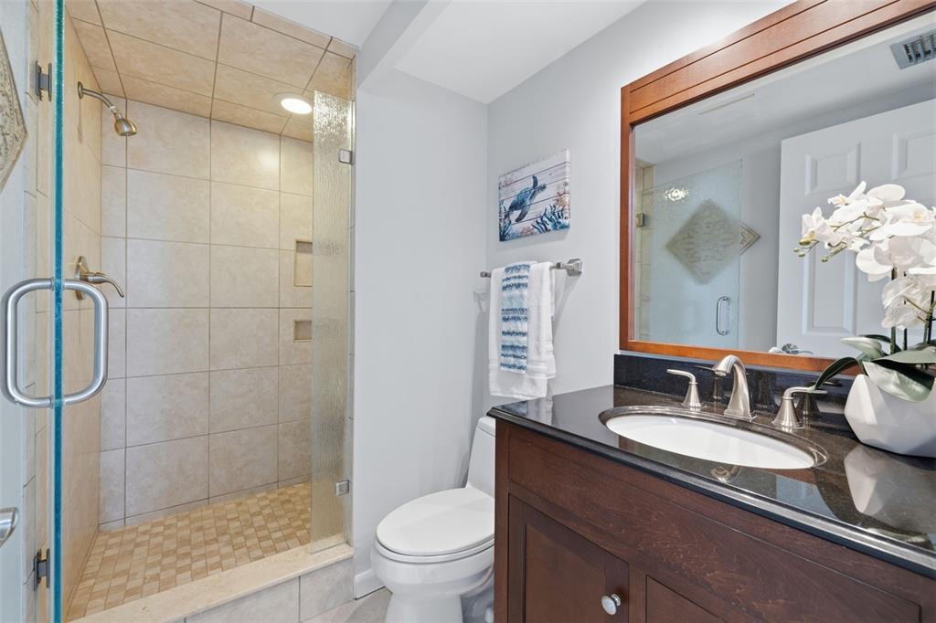 9495 Blind Pass Road, Unit 905 St. Pete Beach, FL 33706 - Photo 21 of 59 a bathroom with a granite countertop sink toilet a mirror and shower