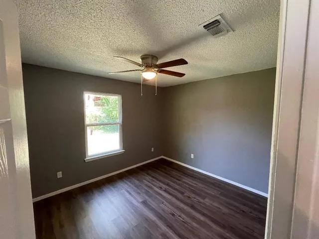 an empty room with wooden floor fan and windows