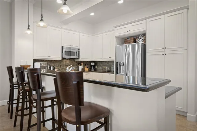 a kitchen with stainless steel appliances granite countertop a stove a refrigerator a sink a dining table and chairs