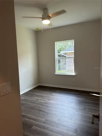 an empty room with wooden floor chandelier fan and windows