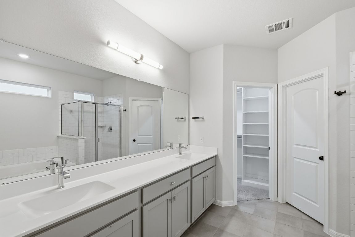 1941 Winston Way Leander, TX 78641 - Photo 18 of 28 Bathroom with a shower stall, double vanity, a walk in closet, a garden tub, and light tile patterned floors